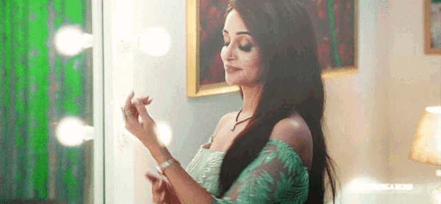 a woman in a green dress is standing in front of a mirror applying makeup .