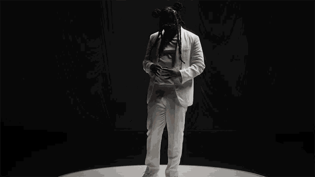 a man in a white suit with dreadlocks is standing on a white surface