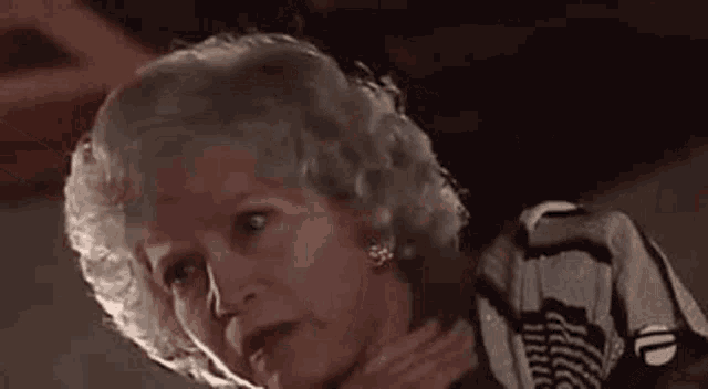 an older woman with gray hair is holding her hand to her neck .