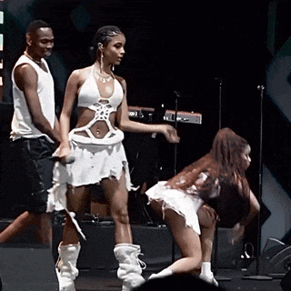 a woman in a white dress is dancing on a stage with two men behind her