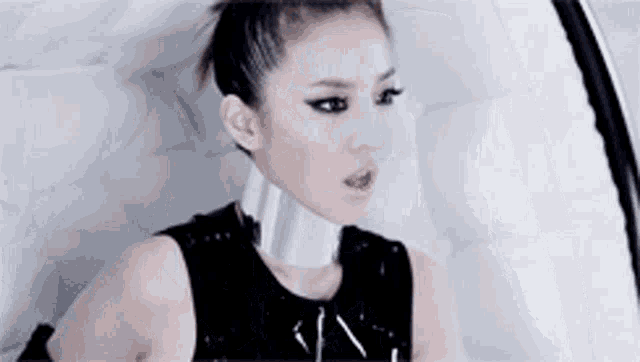 a woman wearing a black top and a silver choker is sitting in a white chair