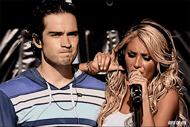 a woman singing into a microphone next to a man with headphones
