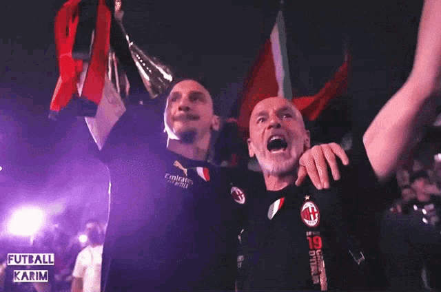 two men holding up a trophy in front of a crowd with the words fotbali karim on the bottom right