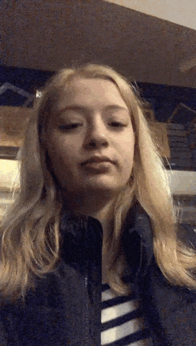 a young woman with blonde hair is wearing a black jacket and a striped shirt .