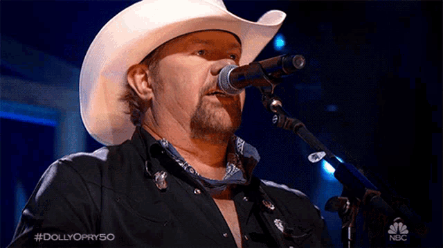 a man in a cowboy hat is singing into a microphone on nbc