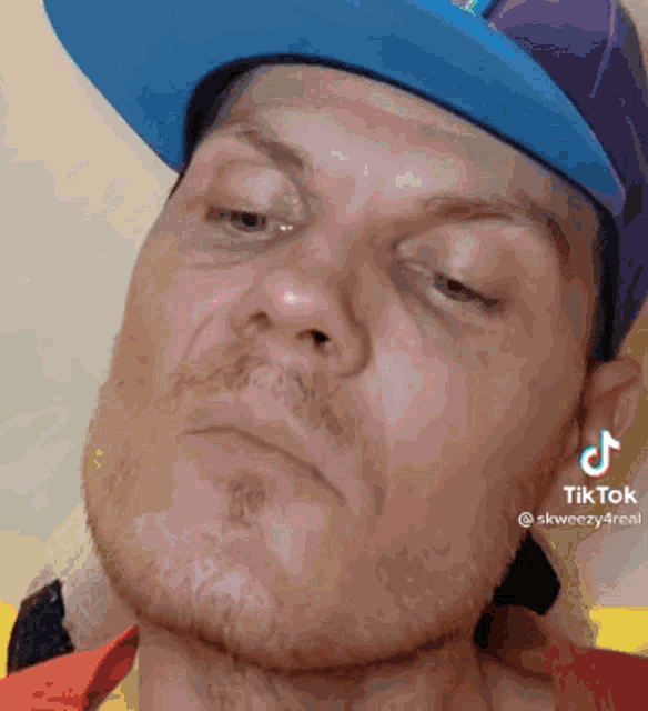 a man wearing a blue and purple hat has a tiktok sticker on his left ear