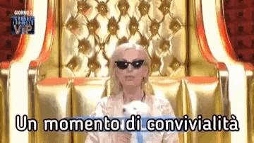 a woman wearing sunglasses is sitting in a chair with the words un momento di convivialità written above her .