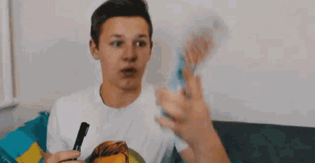 a young boy is sitting on a couch holding a marker and a bottle .