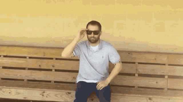 a man sitting on a wooden bench wearing sunglasses