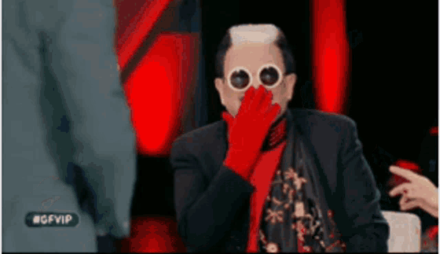 a man wearing red gloves and sunglasses is covering his mouth with his hand