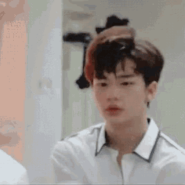a young man in a white shirt is standing in front of a mirror looking at himself .