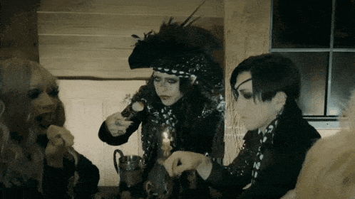 a group of people are sitting around a table and one of them is wearing a feathered hat