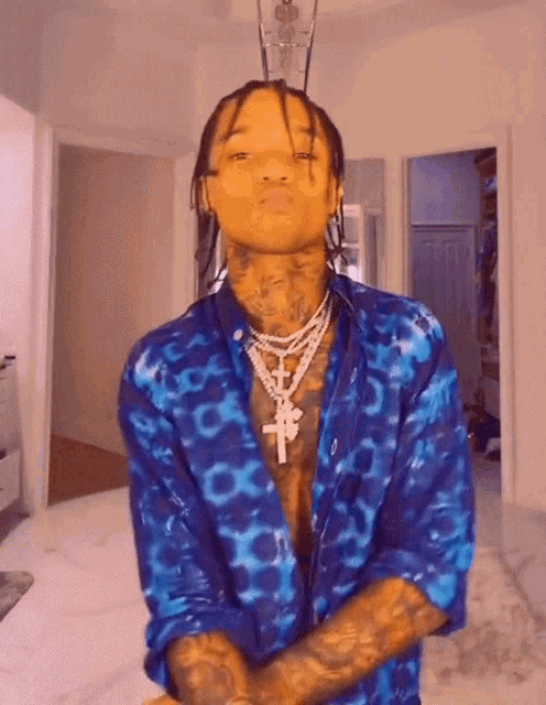 a man wearing a blue shirt and a cross necklace is standing in a room with his arms crossed .