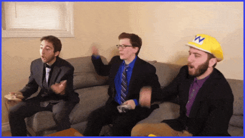 three men are sitting on a couch with one wearing a yellow w hat