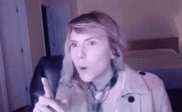 a woman wearing headphones and a trench coat is giving a thumbs up