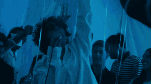 a man in a white shirt is singing into a microphone in a dark room