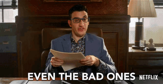 a man sitting at a desk holding a piece of paper with the words even the bad ones netflix behind him