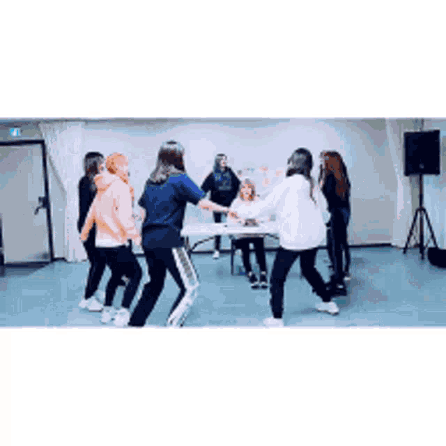 a group of young women are dancing in a circle in front of a table .