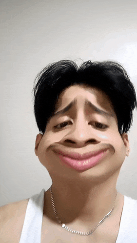 a young man wearing a white tank top and a necklace makes a funny face