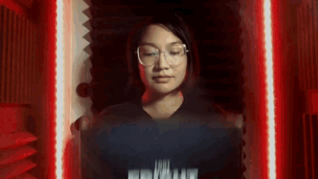 a woman wearing glasses stands in front of a red light behind her