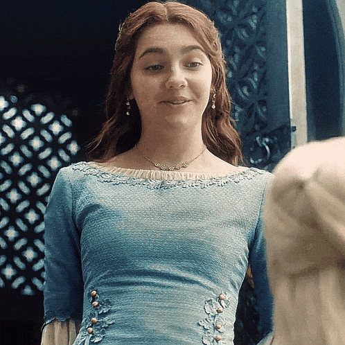 a woman in a blue dress is smiling and wearing a necklace and earrings