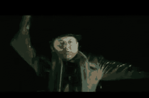 a man in a hat and scarf is standing with his arms outstretched in the dark .