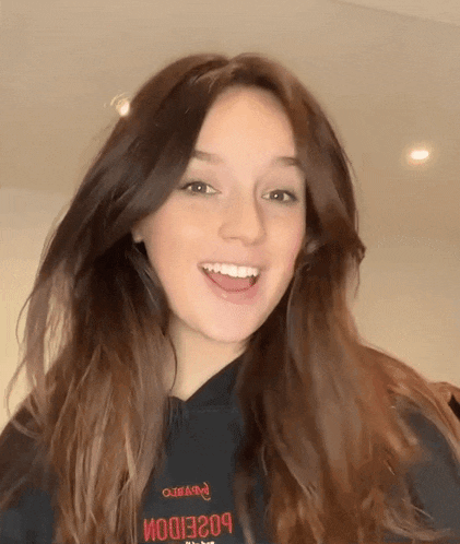 a woman with long brown hair is wearing a black hoodie that says ' poseidon ' on the back .