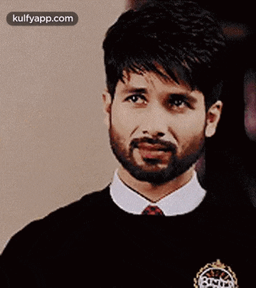 a man with a beard is wearing a black sweater and a white shirt and tie .