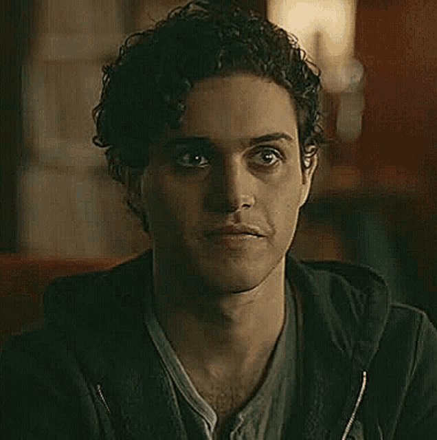 a young man with curly hair is smiling while wearing a black hoodie .