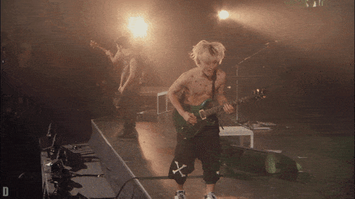 a man without a shirt is playing a guitar on a stage with the letter d in the corner