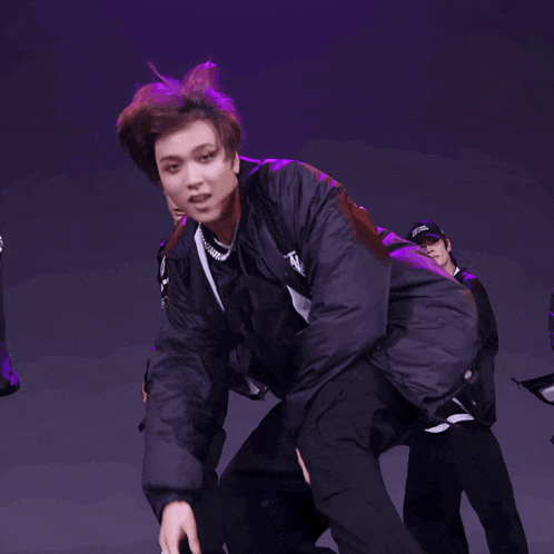 a man in a black jacket with a necklace around his neck is dancing on a stage