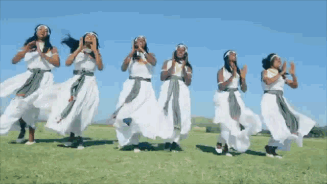 a group of women in white dresses are dancing on a grassy field .