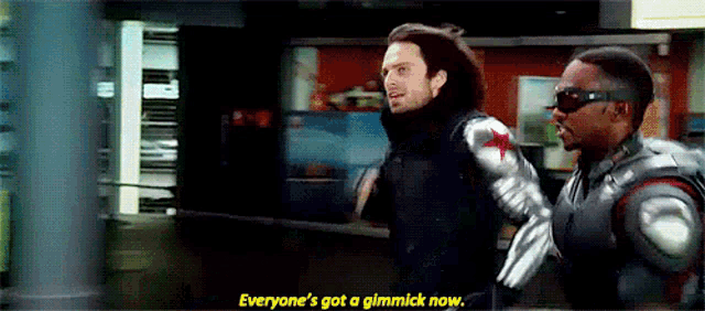 two men in superhero costumes are standing next to each other and talking .