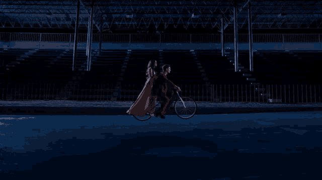 a man and a woman are riding a bicycle in a dark stadium