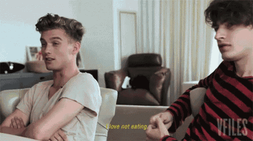 two young men are sitting on a couch and one of them says i love not eating