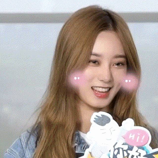 a woman with long blonde hair is smiling and holding a sticker that says hi