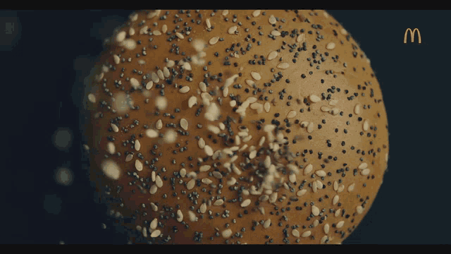 a close up of a bun with sesame seeds and a mcdonalds logo