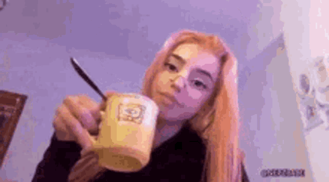 a girl with long blonde hair is holding a cup of coffee with a spoon in it .