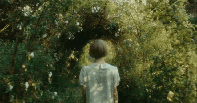 a woman in a white dress is standing in the middle of a forest .
