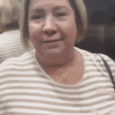 a woman wearing a striped shirt and a necklace is smiling and looking at the camera .