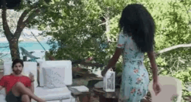 a man is sitting on a couch while a woman in a floral dress is walking towards him .