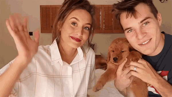 a man and a woman are holding a puppy and waving .