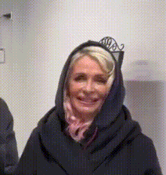 a woman wearing a hooded jacket and a scarf smiles for the camera