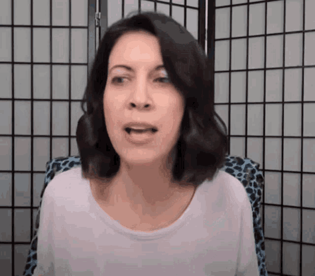 a woman in a white shirt is sitting in front of a screen and making a funny face