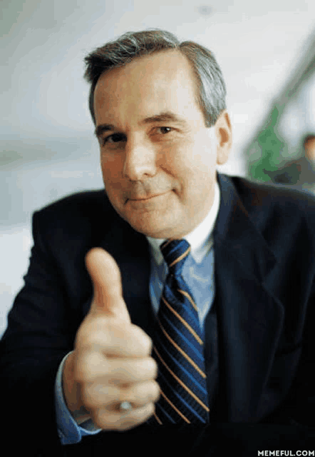 a man in a suit and tie gives a thumbs up sign