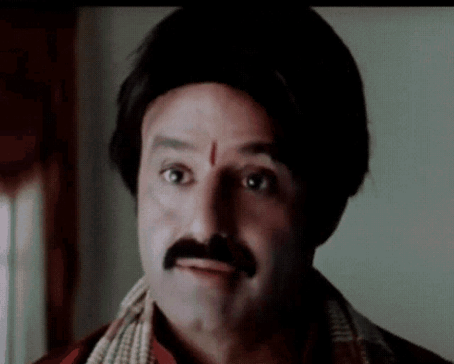 a man with a mustache and a red circle on his forehead