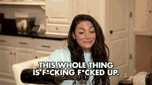 a woman is sitting at a table holding a bottle of wine and saying this whole thing is f * cking f * cked up