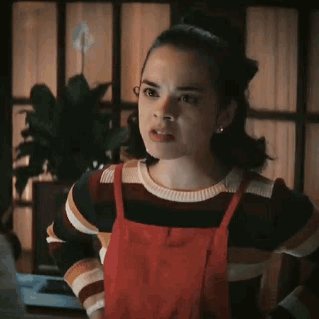 a woman in a striped sweater and red overalls is standing in a room .
