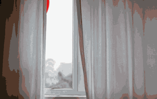 a window with white curtains and a red balloon in the window