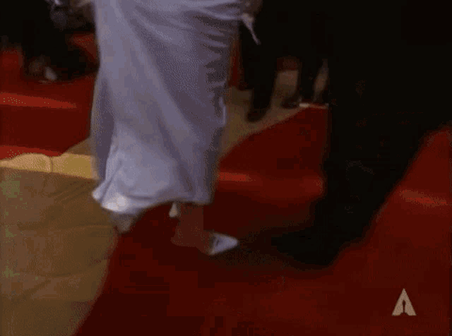 a woman in a white dress is dancing on a red carpet with the letter a in the background